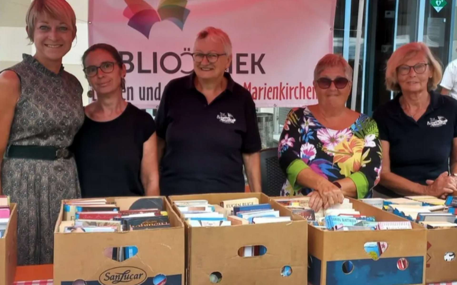 Bücherflohmarkt - Team der Bücherei hinter Tisch mit Bananenschachteln, die mit Büchern gefüllt sind.