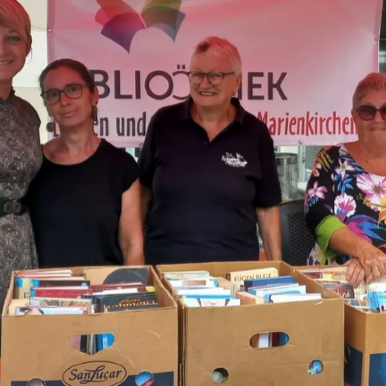 Bücherflohmarkt - Team der Bücherei hinter Tisch mit Bananenschachteln, die mit Büchern gefüllt sind.